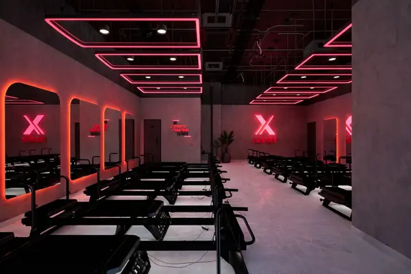 Group fitness studio with rows of equipment under a red linear lighting grid
